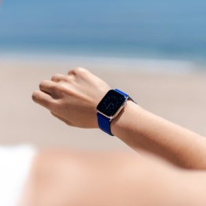 Blueberry Summer-Apple-watch-blue-fluo-band-on-a-feminne-tunned-wrist-with-the-sea-as-background